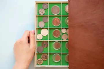 A woman carefully removes a plastic case containing rare antique coins from a wooden box.